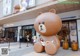 A woman sitting on a giant brown bear statue in front of a store.