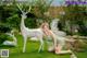 A woman in a green dress sitting on the grass next to a white deer.